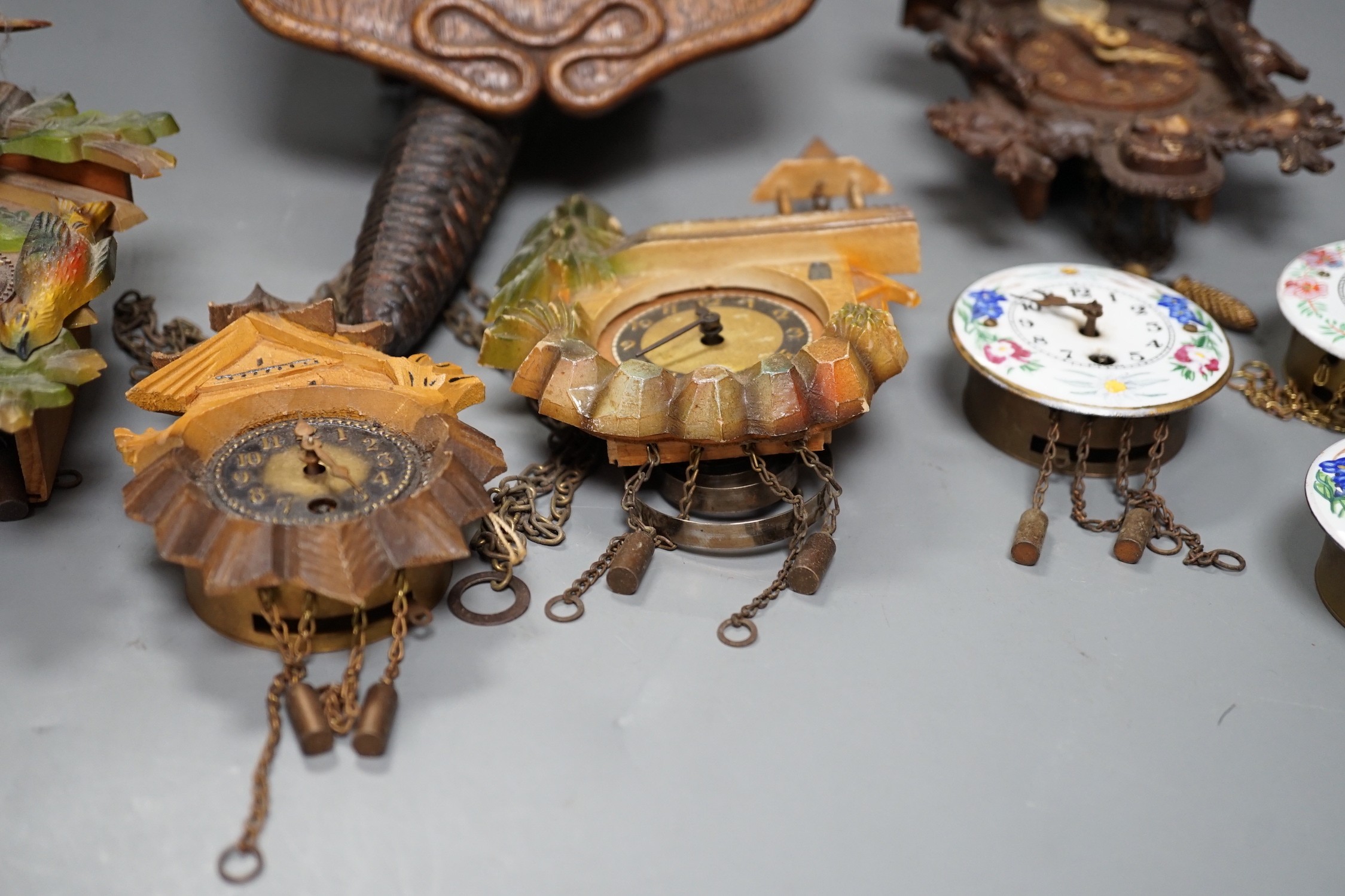 An early 20th century German Jugendstil oak wall timepiece, four miniature Black Forest timepieces and three floral enamelled examples, largest 23cms high